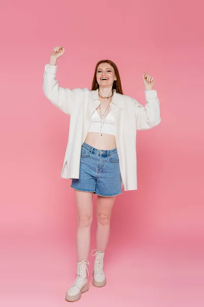 Comprimento total de mulher alegre e elegante olhando para a câmera no fundo rosa — Fotografia de Stock