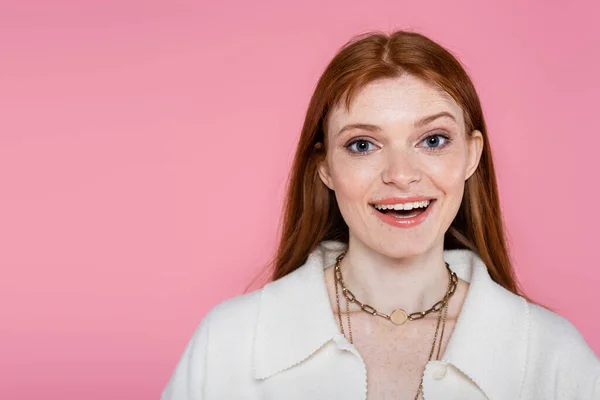 Mujer pecosa positiva en chaqueta y collares mirando a la cámara aislada en rosa - foto de stock