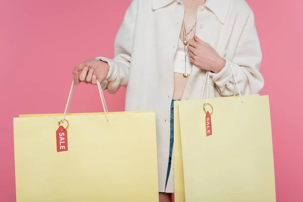 Cropped view of young stylish woman holding shopping bags with price tags and sale lettering isolated on pink — Stock Photo