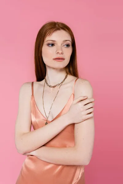 Young freckled and redhead woman in silk dress posing isolated on pink — Stock Photo