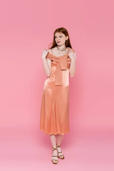 Повна довжина стильної рудої волохатої жінки в шовковій сукні позує на рожевому фоні — стокове фото
