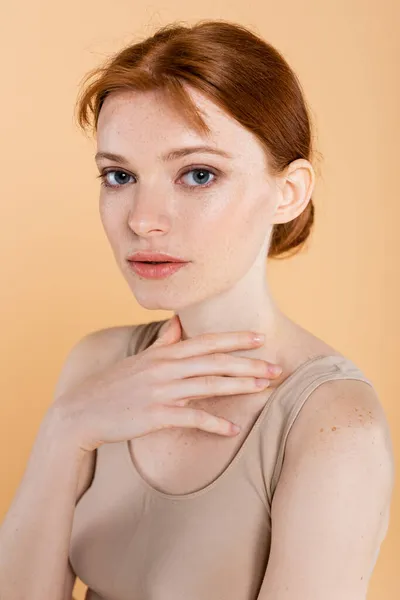 Retrato de mujer joven con piel pecosa mirando a la cámara aislada en beige - foto de stock