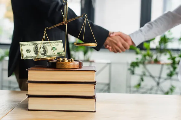 KYIV, UKRAINE - SEPTEMBER 22, 2021: justice scales with dollars on books near cropped business people shaking hands, anti-corruption concept — Stock Photo