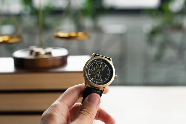 Vista parcial del abogado sosteniendo reloj de pulsera cerca de libros confusos del códice y escalas de justicia, concepto anticorrupción — Stock Photo