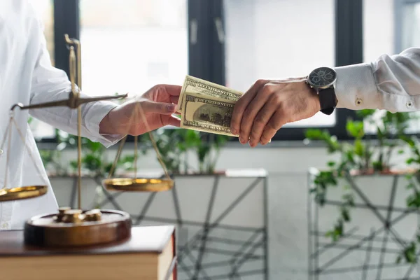 KYIV, UKRAINE - SEPTEMBER 22, 2021: cropped view of businessman giving bribe to woman near justice scales in office, anti-corruption concept — Stock Photo