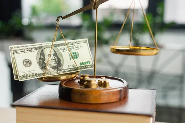 KYIV, UKRAINE - SEPTEMBER 22, 2021: close up view of justice scales with dollars on blurred codex book in office, anti-corruption concept — Stock Photo