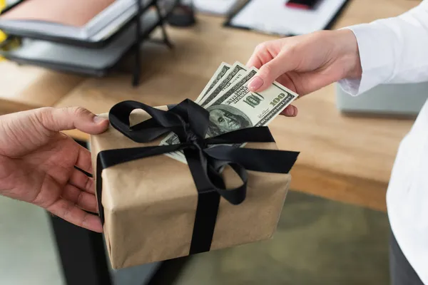 Partial view of woman giving gift box and dollars to businessman in office, anti-corruption concept — Stock Photo