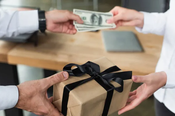 Partial view of businessman giving gift box and blurred dollars to woman, anti-corruption concept — Stock Photo