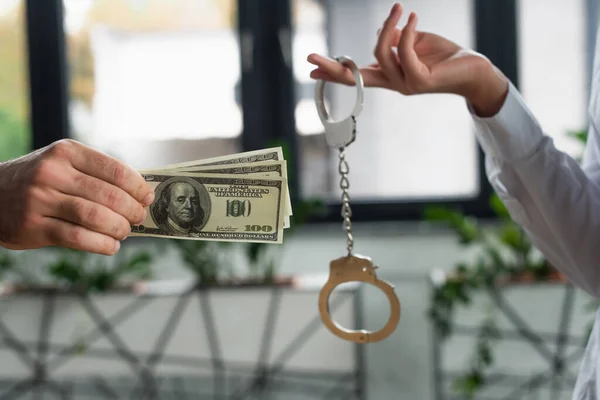 KYIV, UKRAINE - SEPTEMBER 22, 2021: cropped view of woman holding handcuffs near man with dollar banknotes, anti-corruption concept — Stock Photo