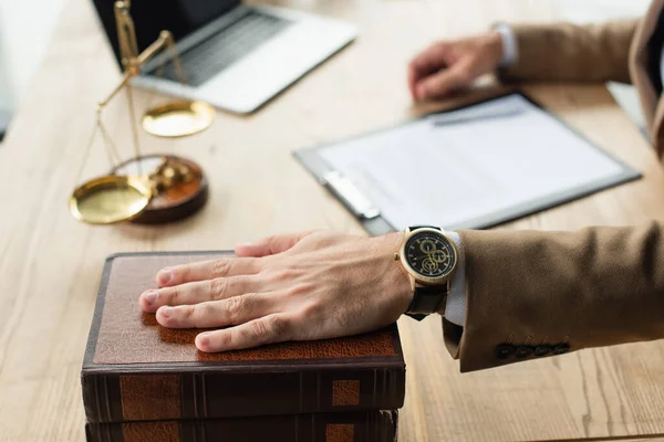 Partial view of lawyer holding hand on codex book near blurred justice scales, anti-corruption concept — Stock Photo