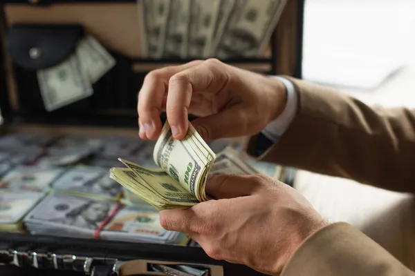 Abgeschnittene Ansicht des Geschäftsmannes, der Geld in der Nähe einer verschwommenen Aktentasche mit Dollars zählt, Anti-Korruptions-Konzept — Stockfoto