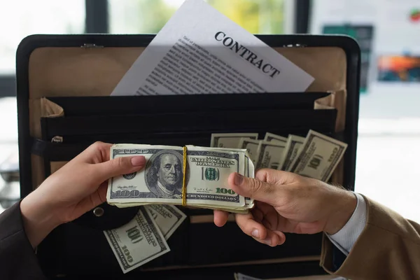 KYIV, UKRAINE - SEPTEMBER 22, 2021: cropped view of business people holding dollars near briefcase with contract, anti-corruption concept — Stock Photo