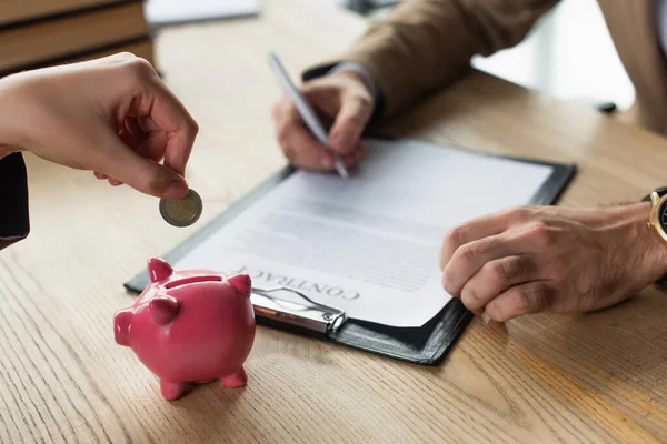 Cropped view of woman putting coin into piggy bank near blurred businessman signing contract, anti-corruption concept — Stock Photo