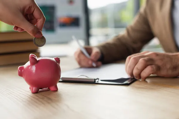 Cropped view of woman holding coin near piggy bank while blurred businessman signing contract, anti-corruption concept — Stock Photo