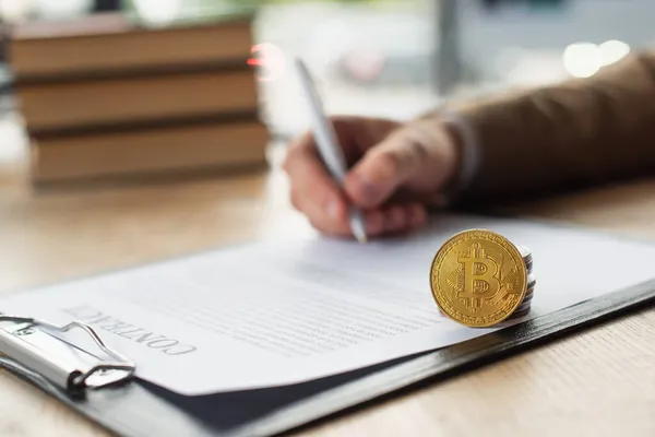 KYIV, UKRAINE - 22 SEPTEMBRE 2021 : recadré d'homme d'affaires flou signature contrat près de l'argent et Bitcoin, concept anti-corruption — Photo de stock