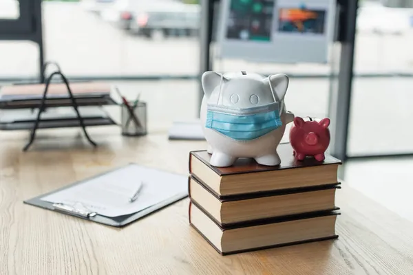 Piggy banks with medical mask on codex books near blurred contract on desk, anti-corruption concept — Stock Photo