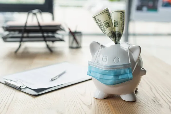 Medizinische Maske auf Sparschwein mit Dollarnoten in der Nähe verschwommenen Vertrag auf dem Schreibtisch, Anti-Korruptions-Konzept — Stockfoto