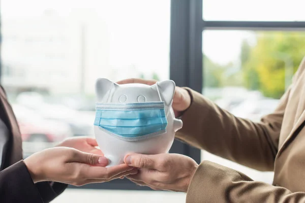 Vue partielle des hommes d'affaires tenant la tirelire dans le masque médical, concept anti-corruption — Photo de stock