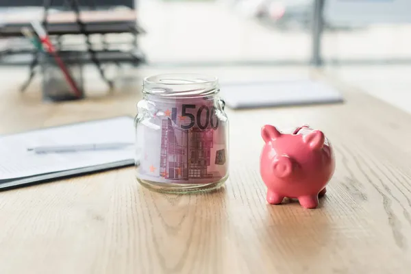 Pot en verre avec billets en euros près de la tirelire sur le bureau, concept anti-corruption — Photo de stock