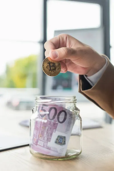 KIEW, UKRAINE - 22. SEPTEMBER 2021: Ausgeschnittene Ansicht eines Geschäftsmannes, der Bitcoin in der Nähe eines Glasgefäßes mit Euro-Banknoten hält, Antikorruptionskonzept — Stockfoto