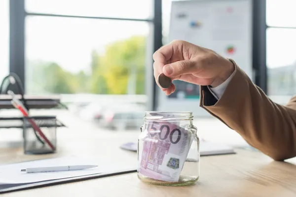 Visão parcial do empresário segurando moeda perto de frasco de vidro com notas de euro no escritório, conceito anti-corrupção — Fotografia de Stock