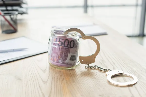 Glass jar with euro banknotes and handcuffs near blurred document, anti-corruption concept — Stock Photo