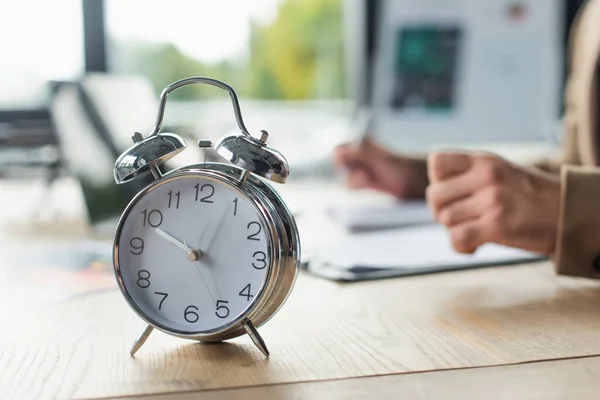 Enfoque selectivo de reloj despertador vintage cerca de hombre de negocios recortado trabajando sobre fondo borroso, concepto anticorrupción - foto de stock