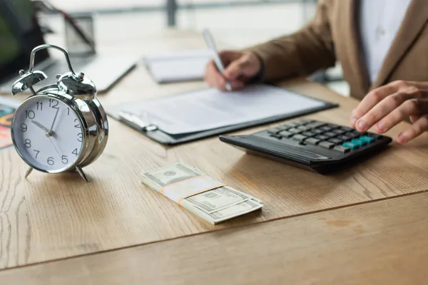 Vista parcial del empresario que firma contrato cerca de dólares, calculadora y despertador, concepto anticorrupción - foto de stock