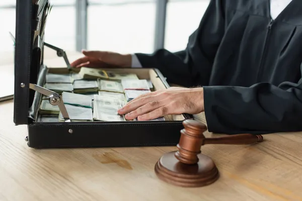 Cropped view of judge near gavel and briefcase with dollar banknotes, anti-corruption concept — Stock Photo