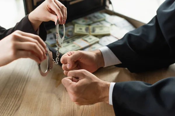 Partial view of woman holding handcuffs near briber and briefcase with money, anti-corruption concept — Stock Photo