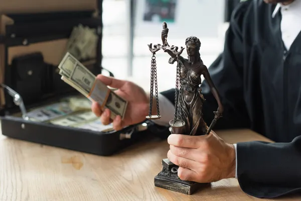 Partial view of lawyer holding themis statue and dollars near blurred briefcase, anti-corruption concept — Stock Photo