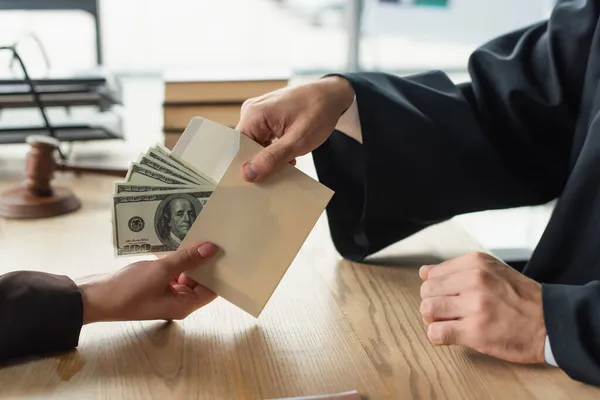 Visión parcial de la mujer dando dinero en sobres para juzgar, concepto anticorrupción - foto de stock