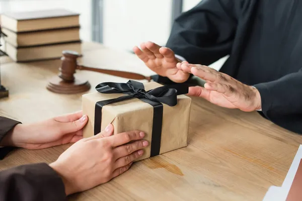 Vista recortada de la mujer con caja de regalo cerca del juez mostrando gesto de basura, concepto anticorrupción - foto de stock