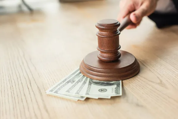 Vue partielle du juge tenant un marteau en bois près des billets en dollars sur le bureau, concept anti-corruption — Photo de stock