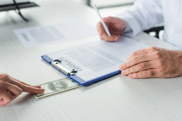 Vue partielle du médecin signant contrat près du patient avec des dollars, concept anti-corruption — Photo de stock