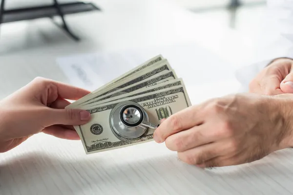 Partial view of doctor with stethoscope near patient with dollar banknotes, anti-corruption concept — Stock Photo