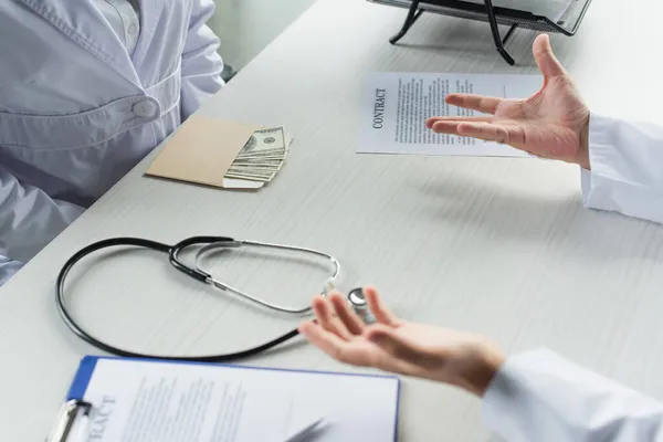 Visão cortada de envelope com dólares perto paciente e médico com palmas abertas, conceito anti-corrupção — Fotografia de Stock