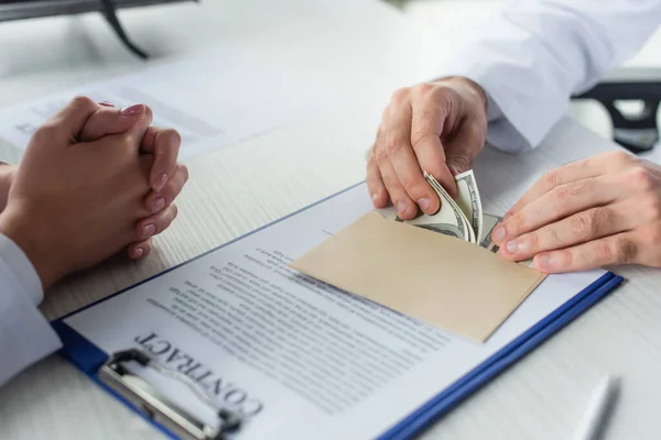 Partial view of doctor counting money near blurred contract and patient with clenched hands, anti-corruption concept — Stock Photo