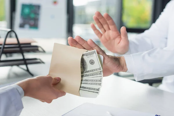 Vista recortada de la mujer sosteniendo soborno cerca del médico mostrando gesto de stop, concepto anticorrupción - foto de stock