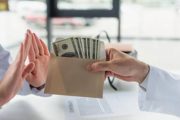 Vista parcial del médico mostrando gesto de desecho cerca de envoltura con soborno, concepto anticorrupción - foto de stock