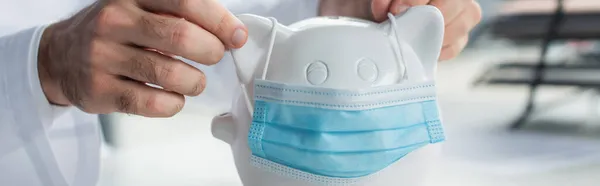 Partial view of doctor putting medical mask on moneybox, anti-corruption concept, banner — Stock Photo