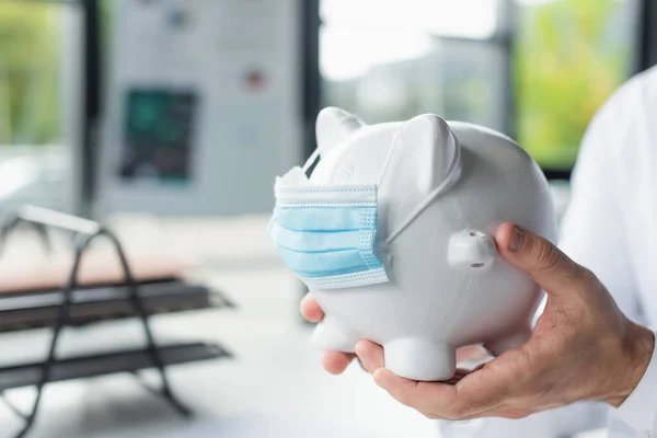 Cropped view of doctor holding piggy bank in medical mask in hospital, anti-corruption concept — Stock Photo