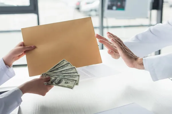 Cropped view of doctor showing stop gesture to patient with envelope and dollars, anti-corruption concept — Stock Photo
