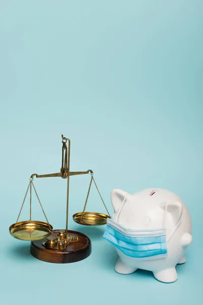 Sparschwein in medizinischer Maske nahe Justizwaage auf blauem Hintergrund mit Kopierraum, Antikorruptionskonzept — Stockfoto