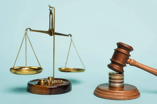 Бронзовые весы правосудия, деревянный молоток и монеты на синем фоне, антикоррупционная концепция — стоковое фото