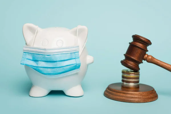 Piggy bank in medical mask near gavel with coins on blue, anti-corruption concept — Stock Photo