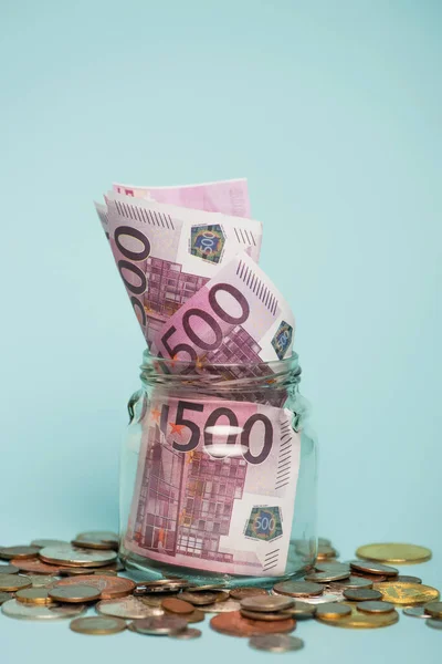 KIEW, UKRAINE - 22. SEPTEMBER 2021: Glas mit Euro-Banknoten in der Nähe von Metallmünzen auf blauem Grund, Antikorruptionskonzept — Stockfoto