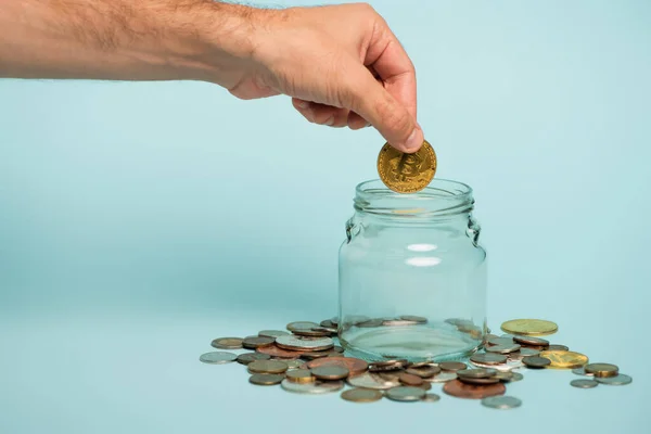 KYIV, UKRAINE - SEPTEMBER 22, 2021: partial view of man putting bitcoin into glass jar near coins on blue, anti-corruption concept — Stock Photo