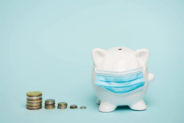 Stapel von Münzen in der Nähe Sparschwein in medizinischer Maske auf blauem Hintergrund mit Kopierraum, Anti-Korruptions-Konzept — Stockfoto