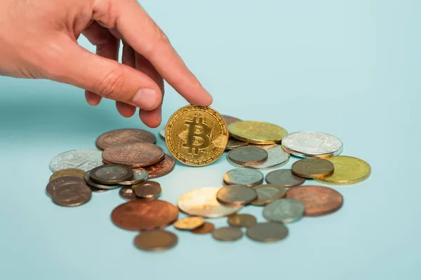 KYIV, UCRANIA - 22 de septiembre de 2021: vista recortada de la mano masculina cerca de bitcoin y monedas en azul, concepto anticorrupción - foto de stock